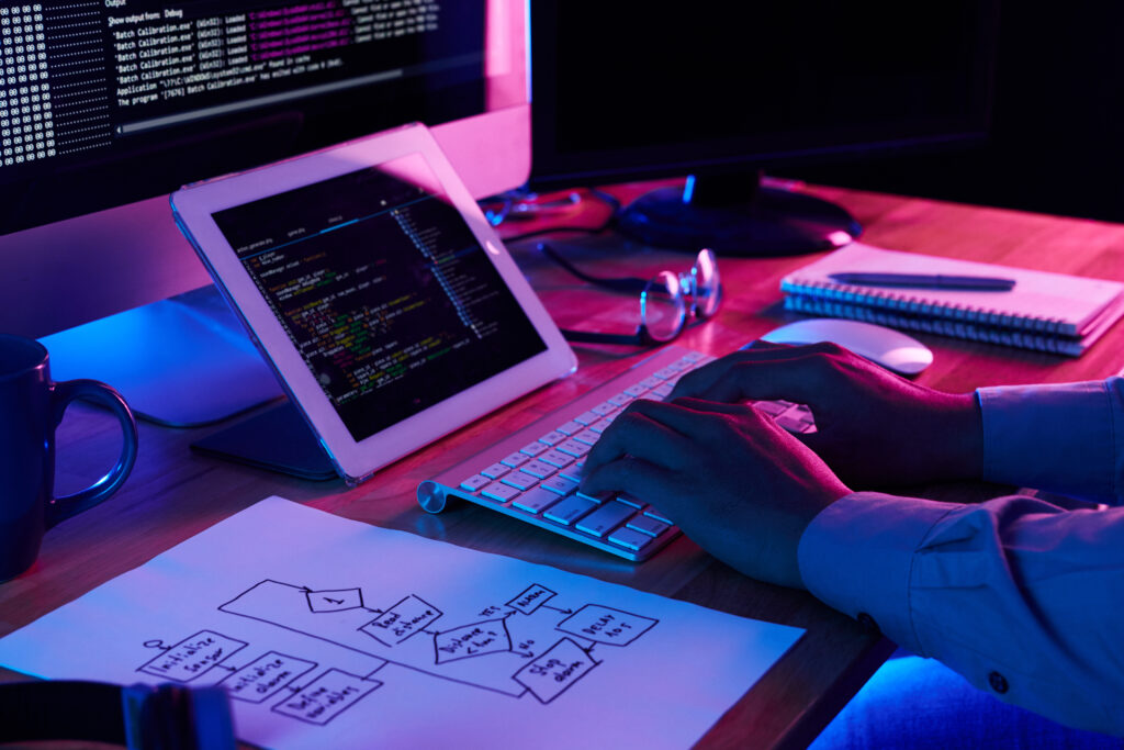 Website designer working on code and user interface at a modern desk with computer, tablet, and flowchart.